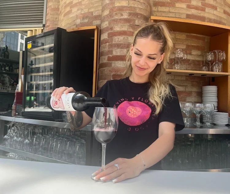 camarera de vino y flores sirviendo una copa de vino tinto en la barra